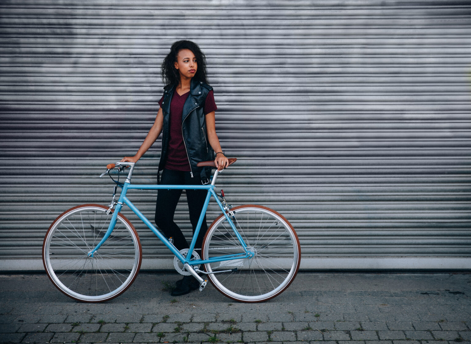 Teen girl standing with her bicycle on a city street African American teenage girl standing on a city street with her fixed gear bicycle in front of urban graffitti