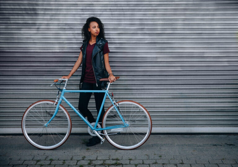 Teen girl standing with her bicycle on a city street African American teenage girl standing on a city street with her fixed gear bicycle in front of urban graffitti